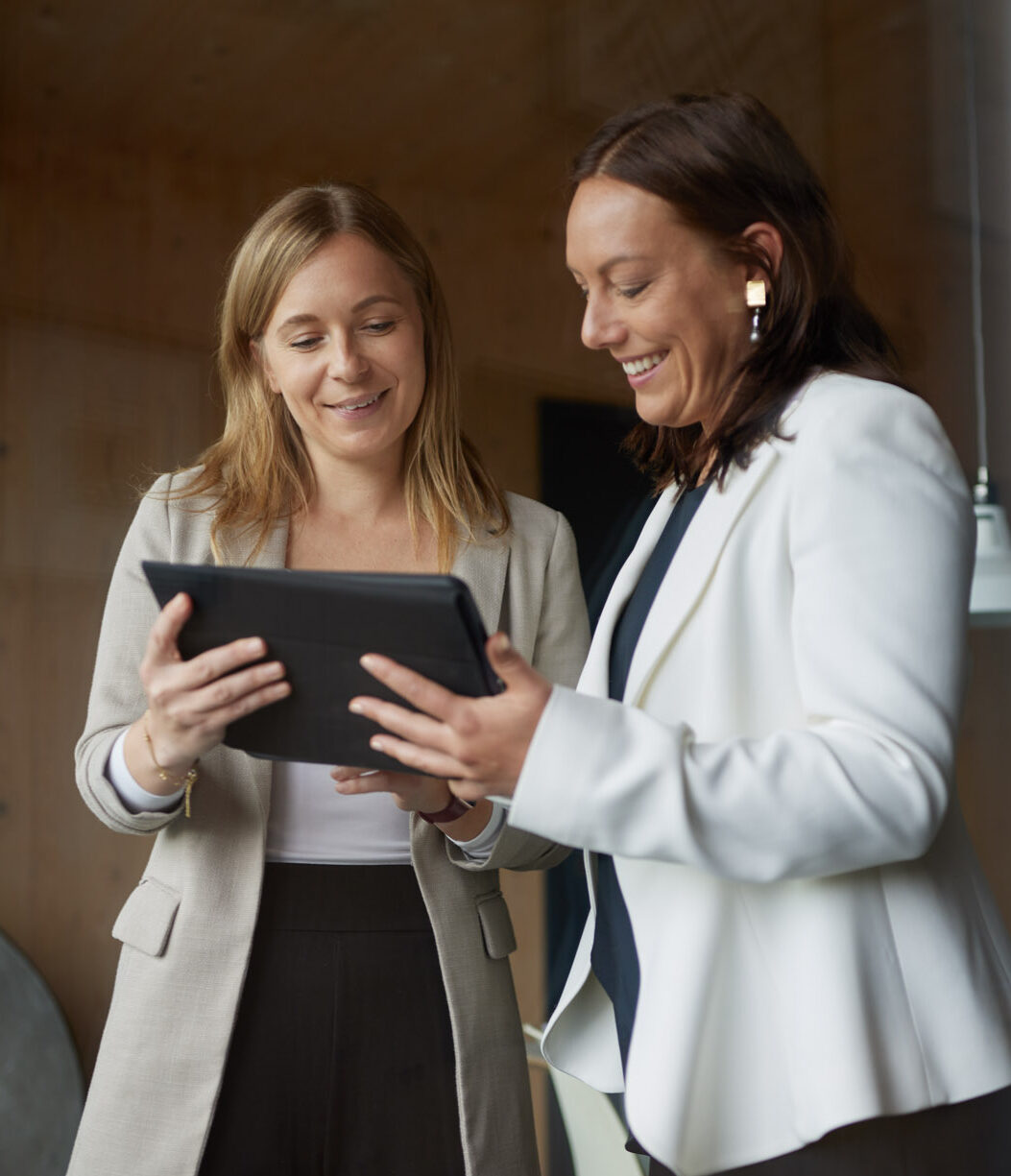 Zwei Frauen lachen gemeinsam bei der Arbeit an einem Tablet – freundlicher Austausch und 1-zu-1 Coaching