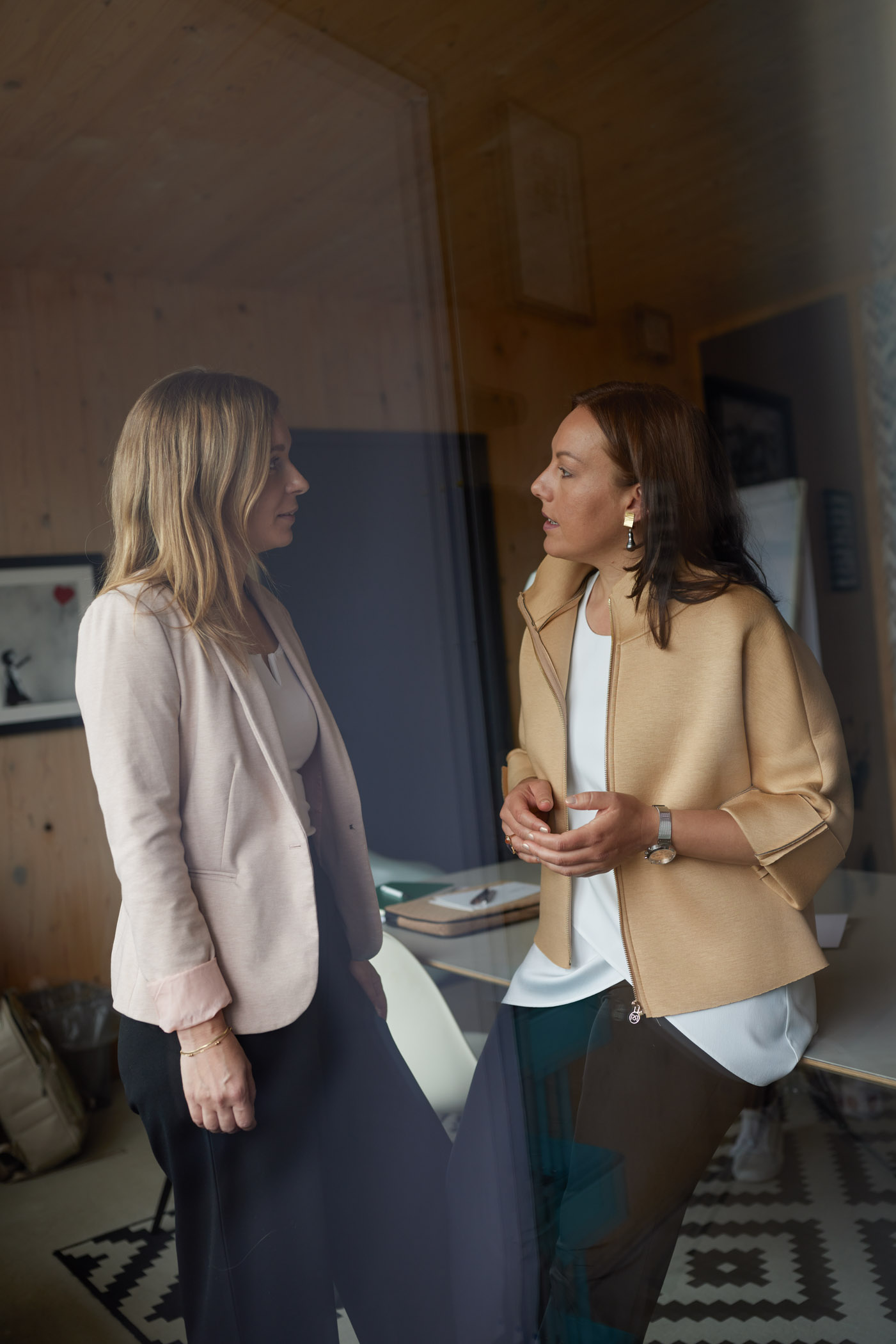 Zwei Frauen stehen im Gespräch am Fenster, in intensiver, respektvoller Kommunikation