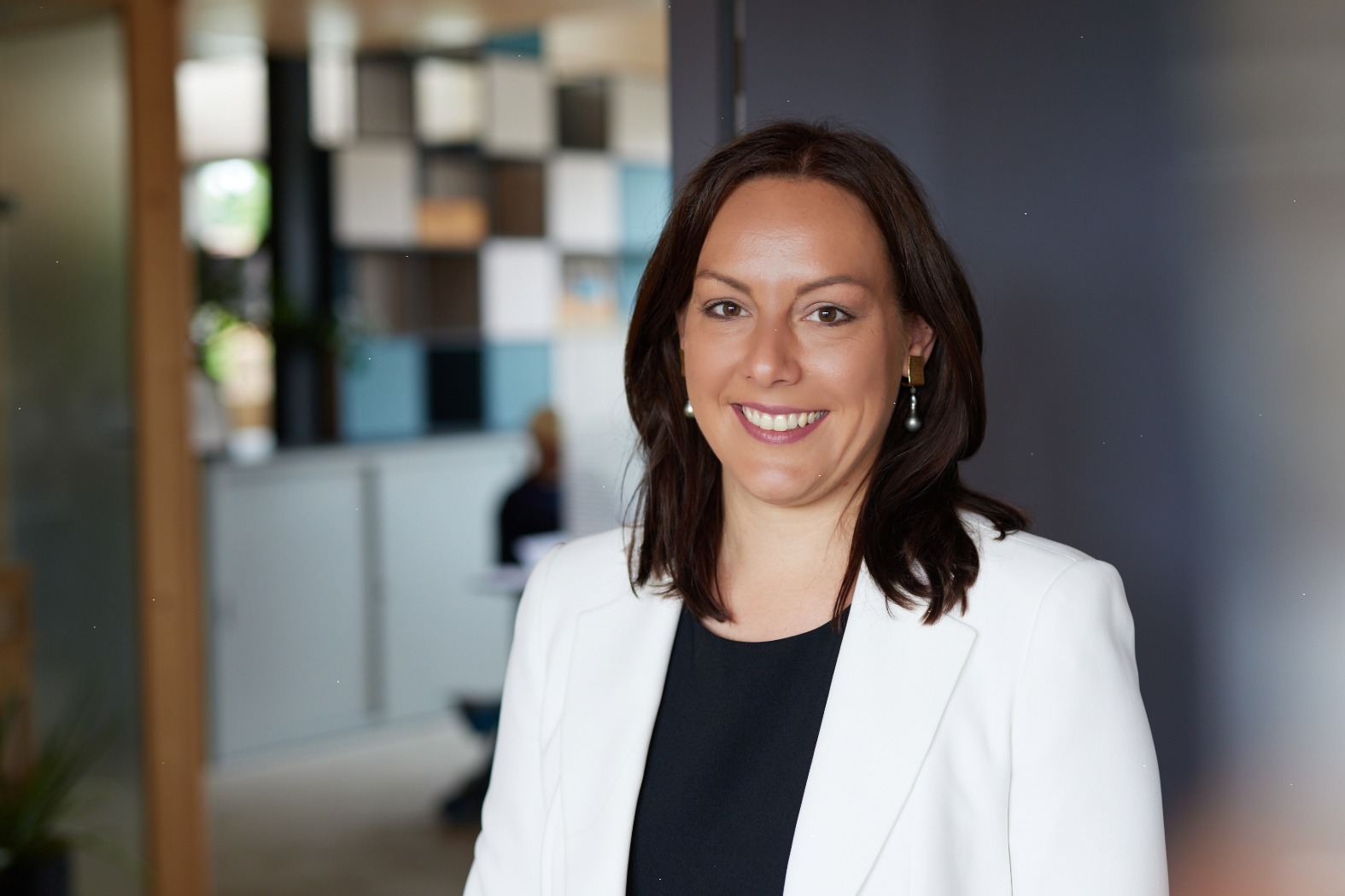 Porträtfoto von Dr. Franziska Zacher, professionell gekleidet, blickt freundlich in die Kamera. Im Hintergrund ein heller, farbenfroher Raum, der eine ruhige und behagliche Atmosphäre vermittelt.