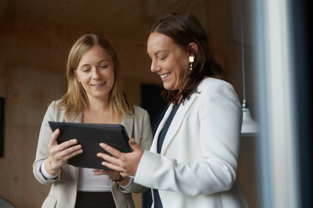 Zwei Frauen stehen nebeneinander und schauen gemeinsam auf ein Tablet, freundlicher Austausch in geschütztem Coaching-Setting