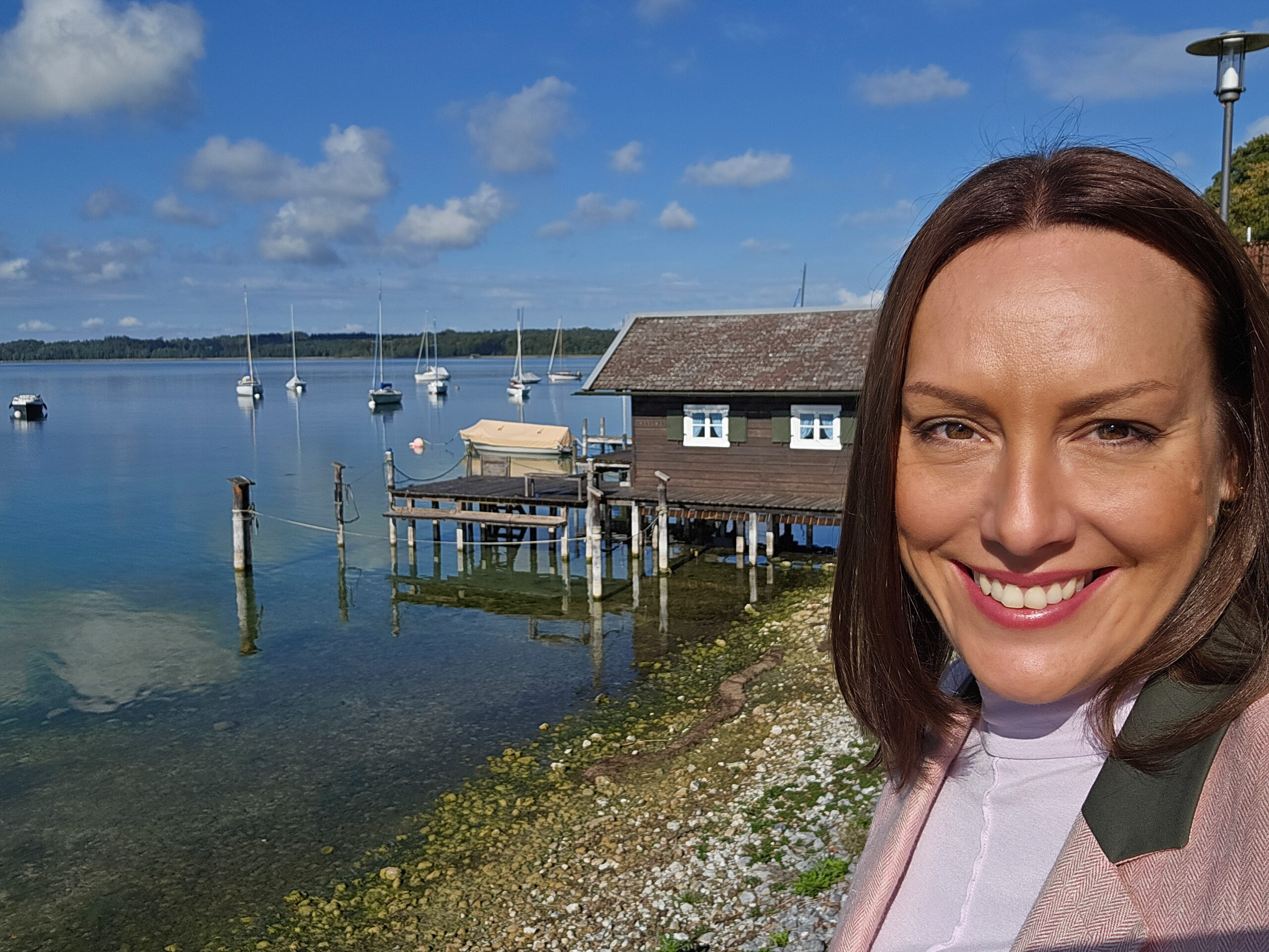 Dr. Franziska Zacher am Starnberger See. Im Hintergrund eine Bootshütte und Segelboote auf dem Wasser.